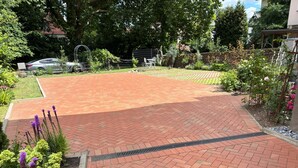 Un'area esterna pavimentata con un motivo in mattoni, circondata da vegetazione e una recinzione in metallo.