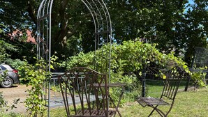 A metal garden chair and table set in a grassy area with a metal trellis structure in the background.