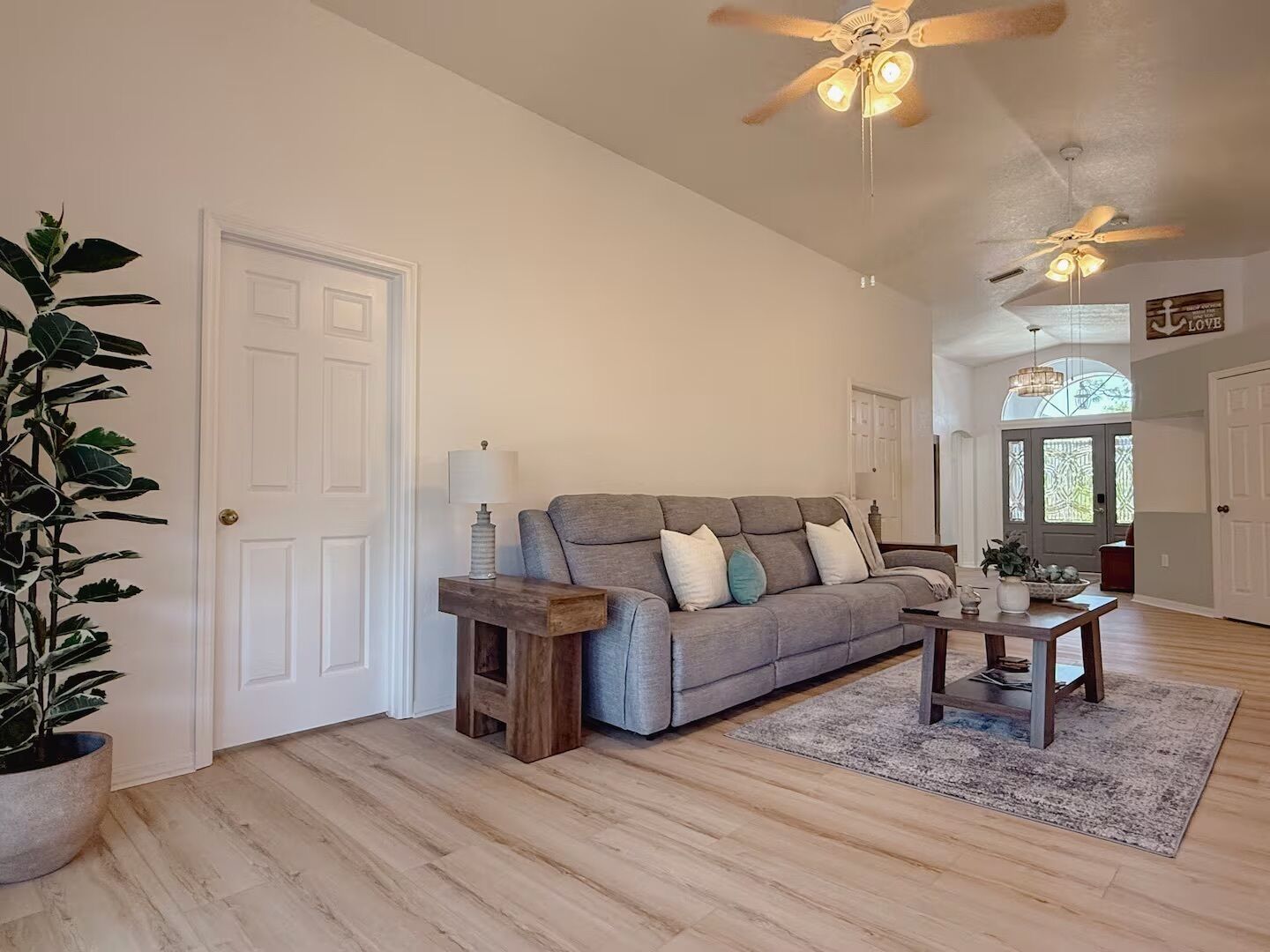 A spacious living room with a grey sofa, wooden coffee table, and a ceiling fan.