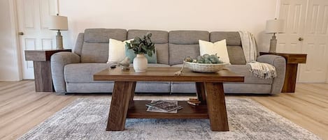 A living room with a grey sofa, a wooden coffee table, and a grey rug.