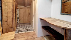 Interior de madera con una puerta que da a un tapete estampado, un espejo y un banco de madera.