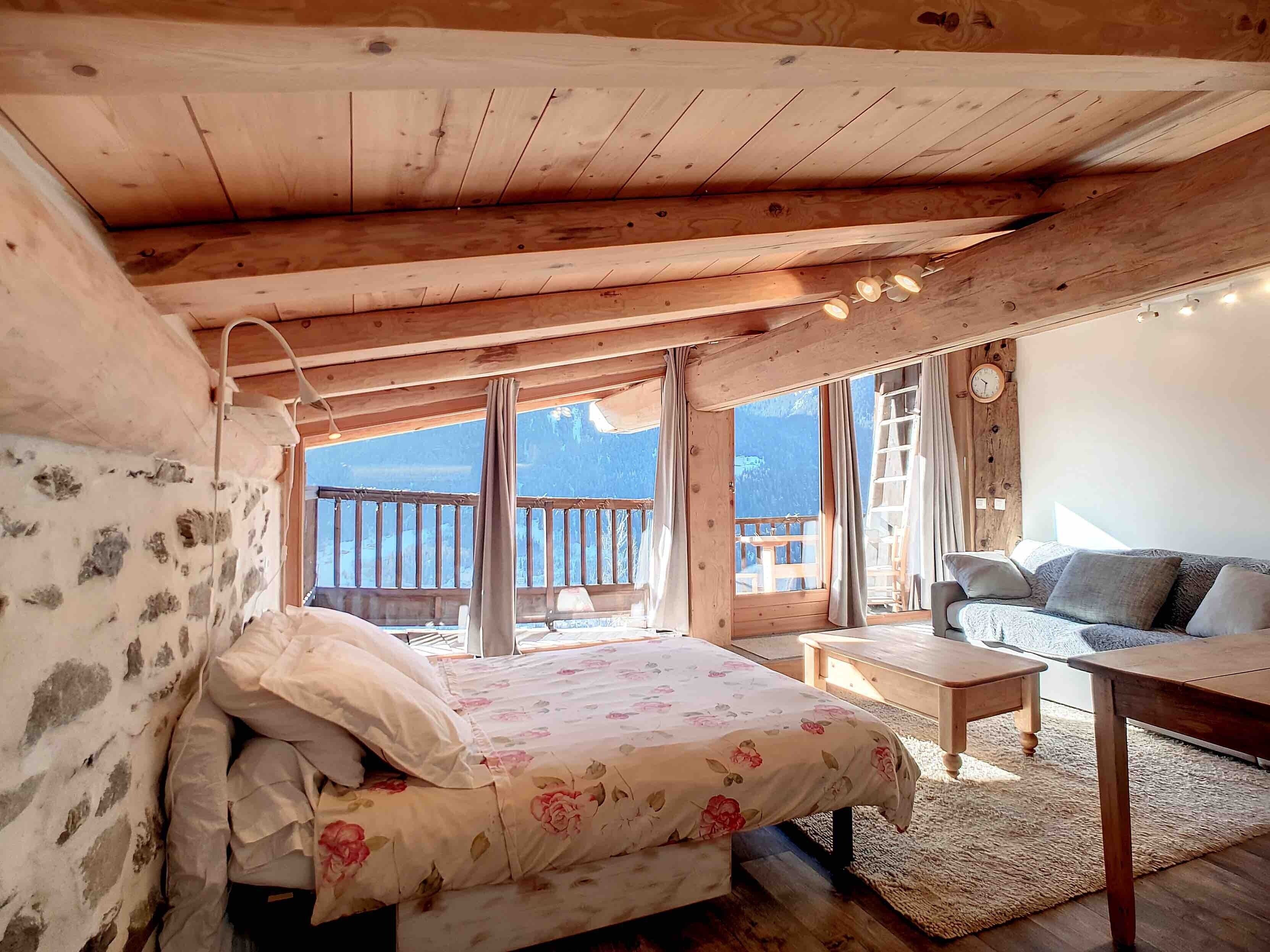 A cozy room with a bed, a sofa, a small table, and a view of the outdoors.