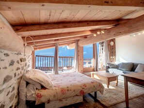 A cozy room with a bed, a sofa, a small table, and a view of the outdoors.