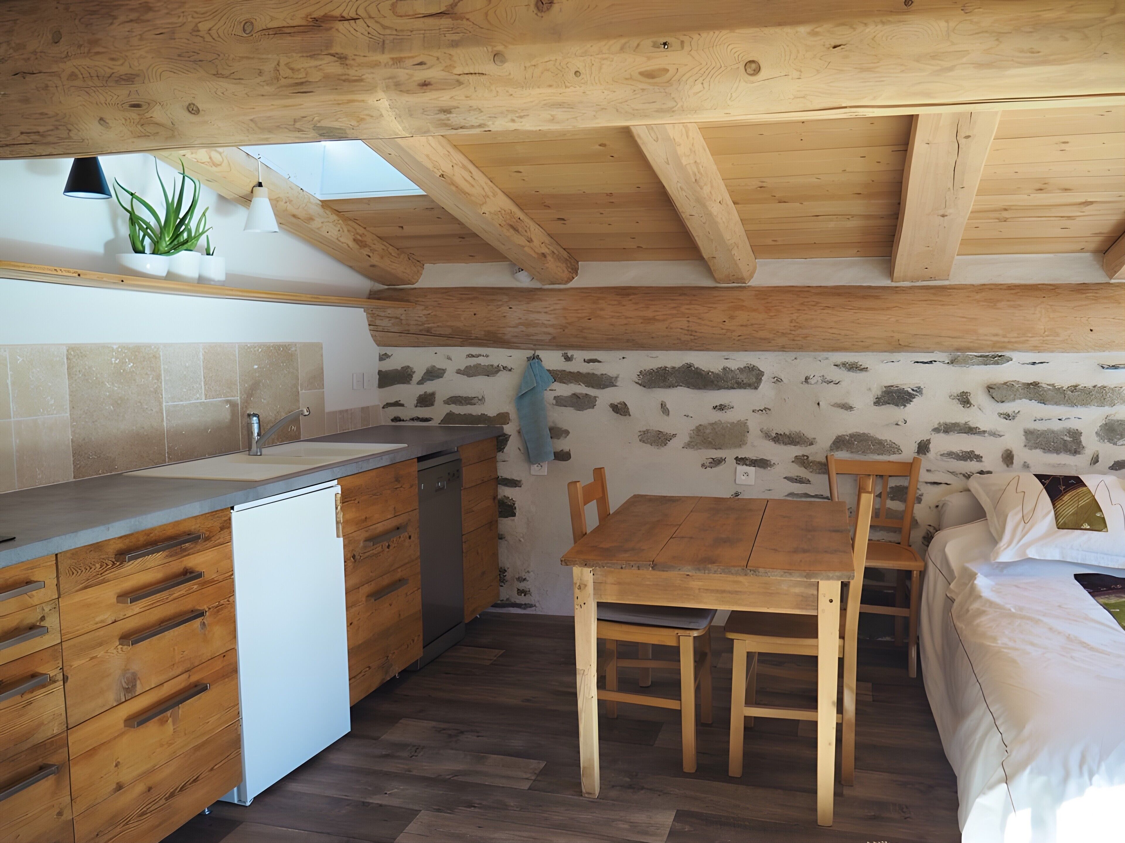 A rustic kitchen with wooden beams, a stone wall, a sink, and a dining area with a table and chairs.