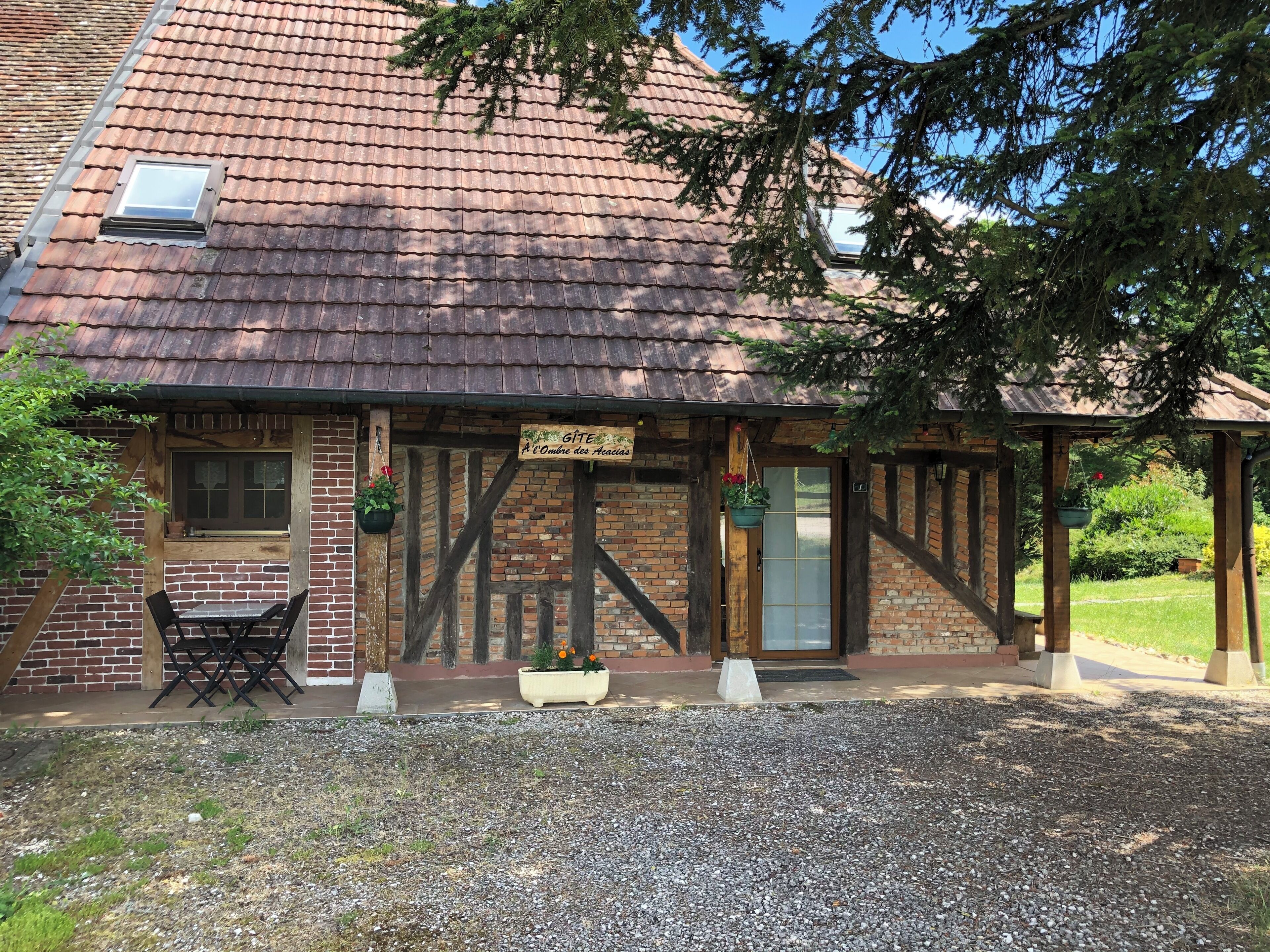 Un bâtiment traditionnel avec un toit en tuiles, une porte en bois et une enseigne indiquant : « GÎTE à l’Ombre des Haies ».