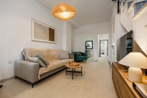 En moderne stue med en sofa, et lille rundt bord og et fjernsyn på et træskab.