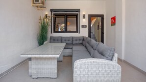 Un espacio exterior moderno con un sofá modular, una mesa de comedor y mobiliario de mimbre.