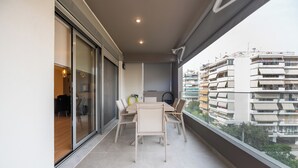 En balkon med et bord og stole, en skydedør samt udsigt til en bygning med flere etager.