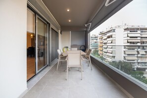 Ein Balkon mit Tisch und Stühlen, eine Glasschiebetür und Blick auf ein mehrgeschossiges Gebäude.