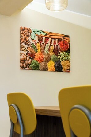 Ein Essbereich mit Tisch und Stühlen, ein Wandbild mit Gewürzen und einer Deckenleuchte.