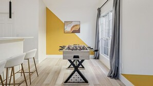 A modern kitchen with a foosball table, bar stools, and a yellow accent wall. - Fireside Retreat| Sleeps 10 | Foosball | Fire pit (Grand Prairie)