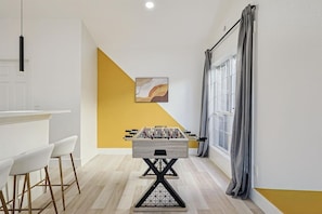 Een moderne keuken met een tafelvoetbaltafel, barstoelen en een gele accentmuur.