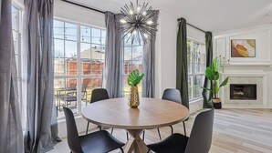 A modern dining room with a round table, black chairs, a pineapple centerpiece, and large windows with curtains. - Fireside Retreat| Sleeps 10 | Foosball | Fire pit (Grand Prairie)