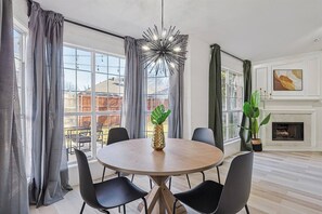 Een moderne eetkamer met een ronde tafel, zwarte stoelen, een ananas als decoratie en grote ramen met gordijnen.