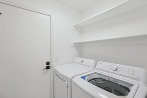 Een wasruimte met een voorlader wasmachine en droger, een witte deur en een plank boven de droger.
