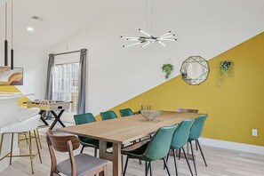 Ein Essbereich mit einem Holztisch, stuhlartigen Sitzgelegenheiten in Türkis und einer modernen Pendelleuchte.