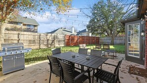 A backyard with a grill, outdoor table, chairs, and a wooden fence. - Fireside Retreat| Sleeps 10 | Foosball | Fire pit (Grand Prairie)