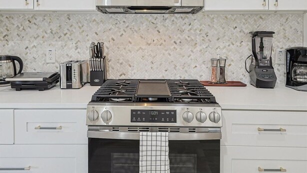 A modern kitchen with a stainless steel stove, a microwave above it, and various appliances like a coffee maker and toaster. - Fireside Retreat| Sleeps 10 | Foosball | Fire pit (Grand Prairie)
