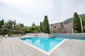 Ein rechteckiger Pool mit Fliesenveranda, umgeben von Bäumen und einem Gebäude im modernen Stil.