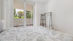 Et soveværelse med en stor seng, en skydedør til en balkon og et sort metalstativ mod væggen.
