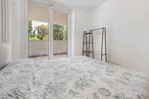 Ein Schlafzimmer mit einem großen Bett, einer Schiebetür zum Balkon und einem schwarzen Metallregal an der Wand.