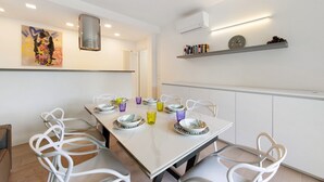 Et moderne spiseområde med et langt bord, hvide stole og farveret glasværk.