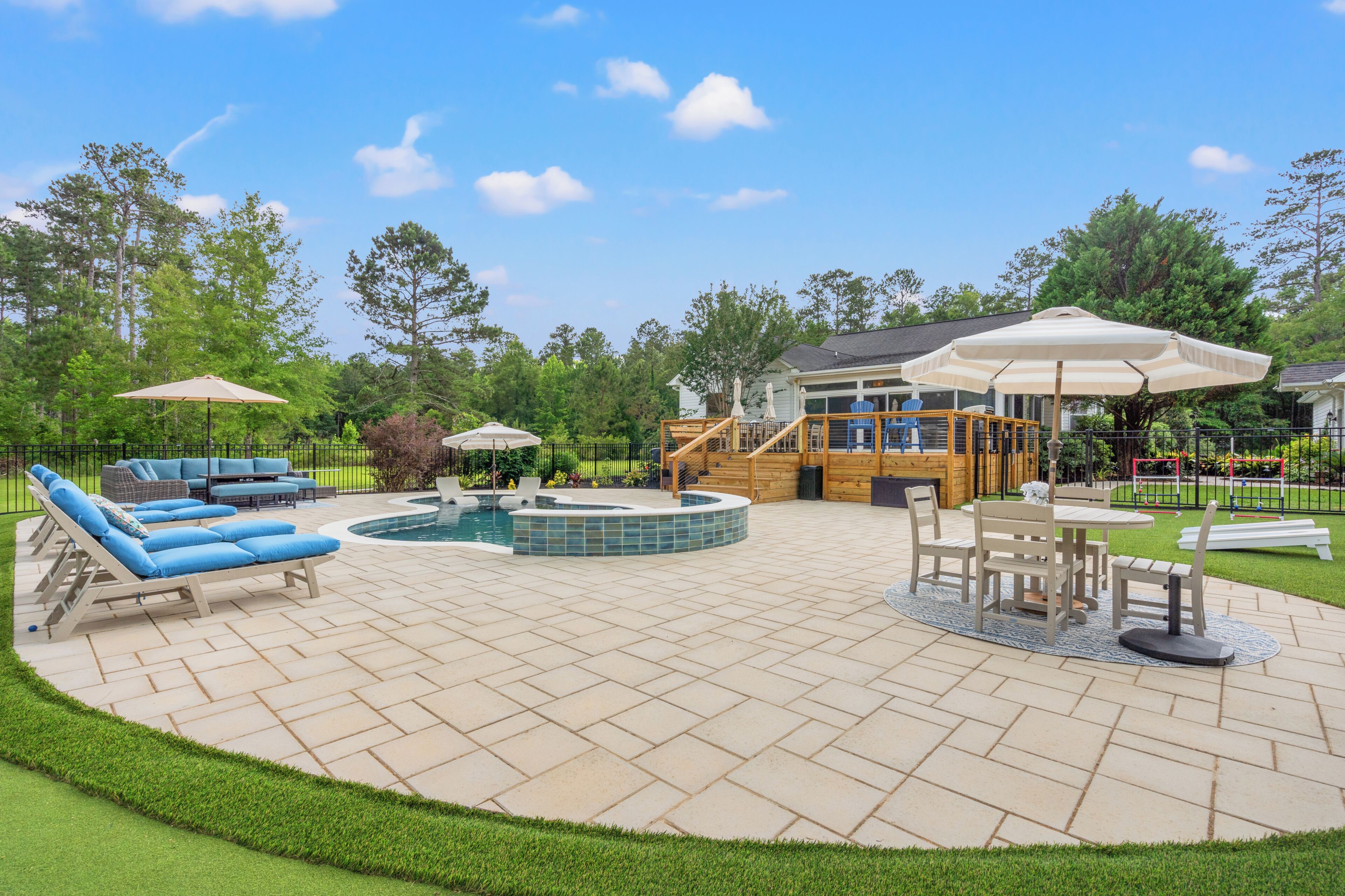 Un patio trasero con piscina, muebles de exterior y una terraza de madera.