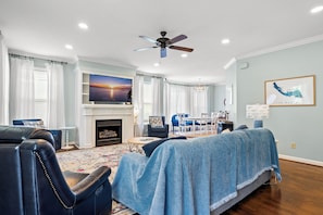 A living room with a fireplace, a ceiling fan, and a large window with curtains. - Beautiful-Lakefront Farmhouse Retreat w/ Pool (Summerton)
