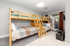 A bunk bed room with a ladder, a small table with a TV, and a sliding glass door to the outside. - Big Water Lodge | Hot Tub, Fire Pit, & Lake Views (Macon)