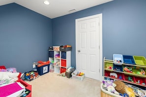A room with a blue wall, a white door, and shelves with various toys and storage bins. - Big Water Lodge | Hot Tub, Fire Pit, & Lake Views (Macon)