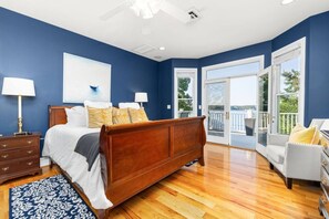 A bedroom with a wooden bed, a nightstand, a dresser, a large window, and a view of the outdoors. - Big Water Lodge | Hot Tub, Fire Pit, & Lake Views (Macon)