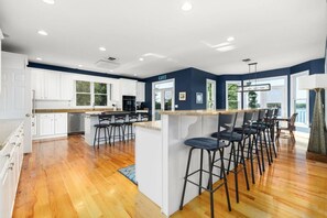 A modern kitchen with white cabinets, a central island with bar stools, and a view of the outdoors. - Big Water Lodge | Hot Tub, Fire Pit, & Lake Views (Macon)