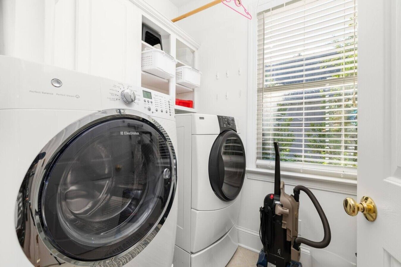 A laundry room with two front-loading washing machines, a dryer, and a vacuum cleaner.