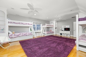 A child's bedroom with bunk beds, a purple rug, a white desk, and a ceiling fan. - Big Water Lodge | Hot Tub, Fire Pit, & Lake Views (Macon)