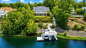 A lakeside property with a dock, a large house, and lush greenery. - Big Water Lodge | Hot Tub, Fire Pit, & Lake Views (Macon)