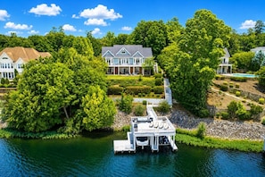 A lakeside property with a dock, a large house, and lush greenery. - Big Water Lodge | Hot Tub, Fire Pit, & Lake Views (Macon)