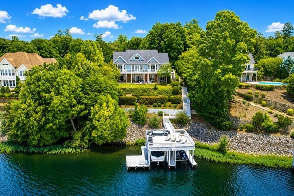 A lakeside property with a dock, a large house, and lush greenery. - Big Water Lodge | Hot Tub, Fire Pit, & Lake Views (Macon)