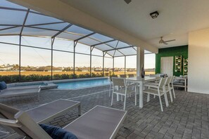 Ein überdachter Außenbereich mit Pool, Liegestühlen und einem Tisch mit Stühlen.