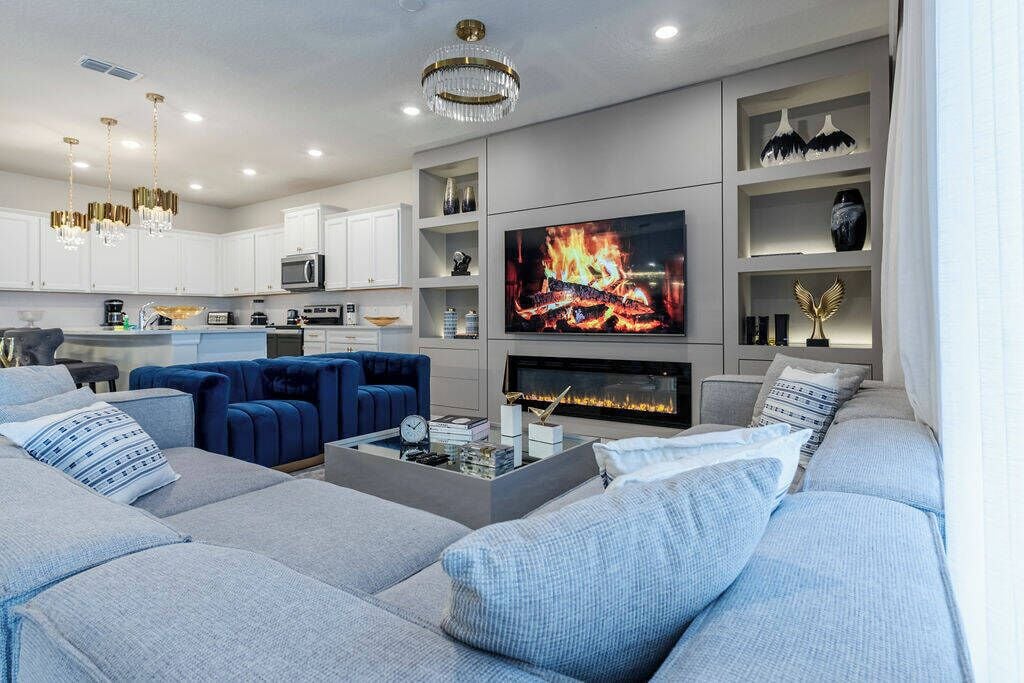 A modern living room with a fireplace, a television, and a kitchen area in the background.
