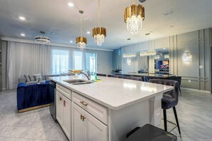Une cuisine moderne dotée d’un îlot central, de luminaires suspendus et d’un coin repas avec un téléviseur.