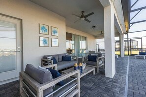 A covered outdoor seating area with a sofa, coffee table, and chairs, a ceiling fan, and framed artwork on the wall. - 10BR house with private pool in Windsor Island (Davenport)