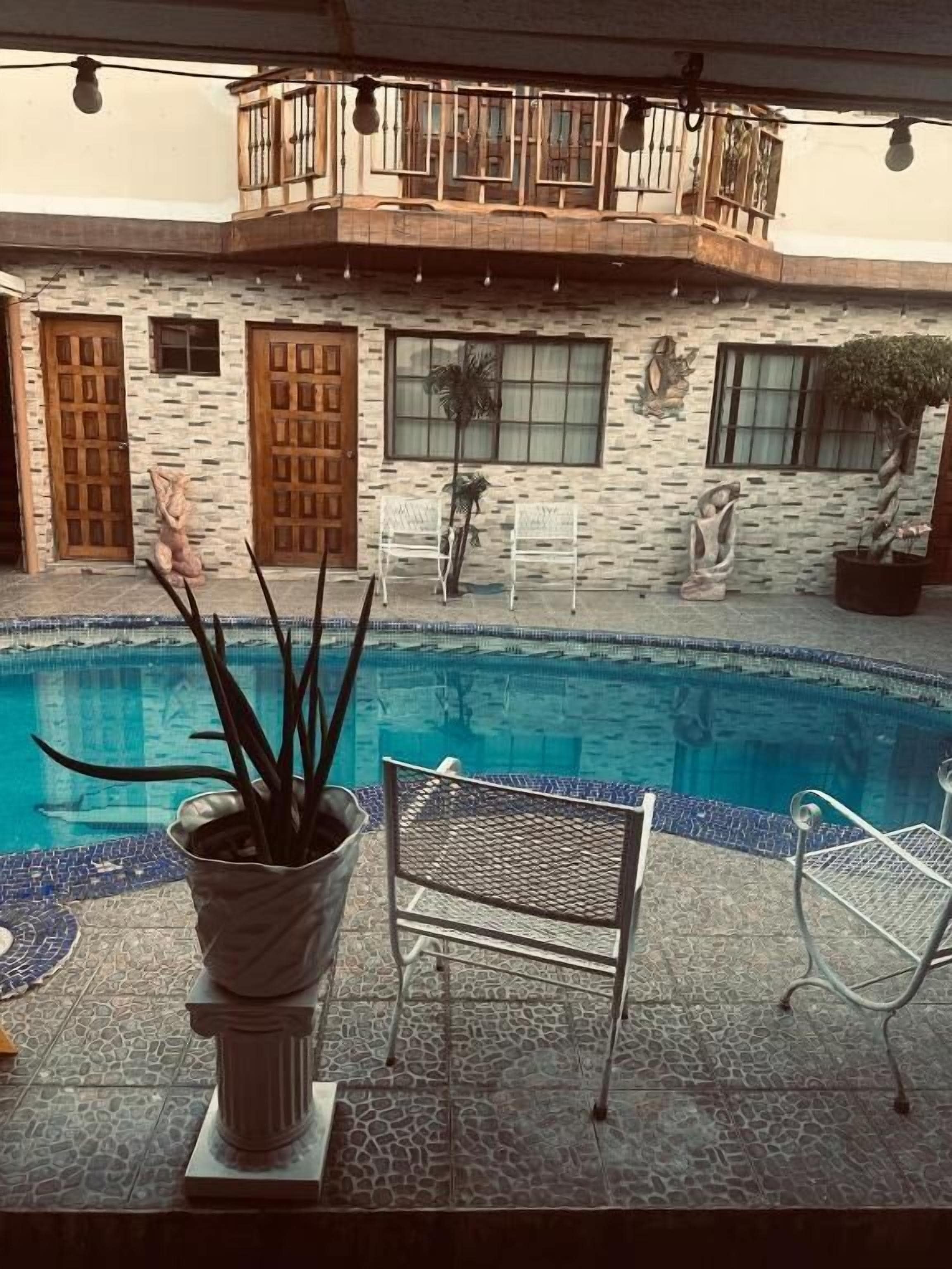 Une piscine avec une façade en pierre, un pot de fleurs et deux chaises en métal.