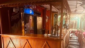 Un espace bar avec un comptoir en bois, un coin salon avec une chaise, et un réfrigérateur Pepsi bien visible.