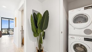 Een moderne wasruimte met een Bosch wasmachine, een grote kamerplant en uitzicht op de stad door een glazen deur.
