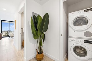 A modern laundry room with a Bosch washing machine, a large potted plant, and a view of the city through a glass door. - Miami Beach Luxury Stay Balcony Sea Views & Pool (Miami Beach)