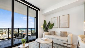 Een moderne woonkamer met een bank, salontafel en stoelen, grote ramen met uitzicht op de stad, en een balkon met een stoel.