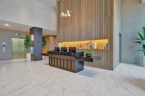 A modern reception desk with a wooden panel backdrop, a marble floor, and a hanging light fixture. - Miami Beach Luxury Stay Balcony Sea Views & Pool (Miami Beach)