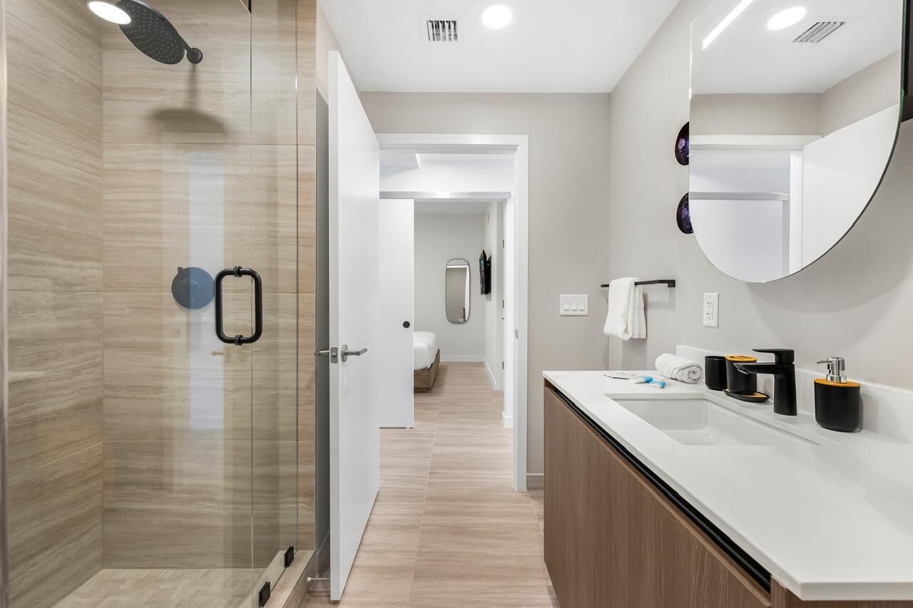 A modern bathroom with a glass shower enclosure, a white sink with black and gold fixtures, and a large mirror.