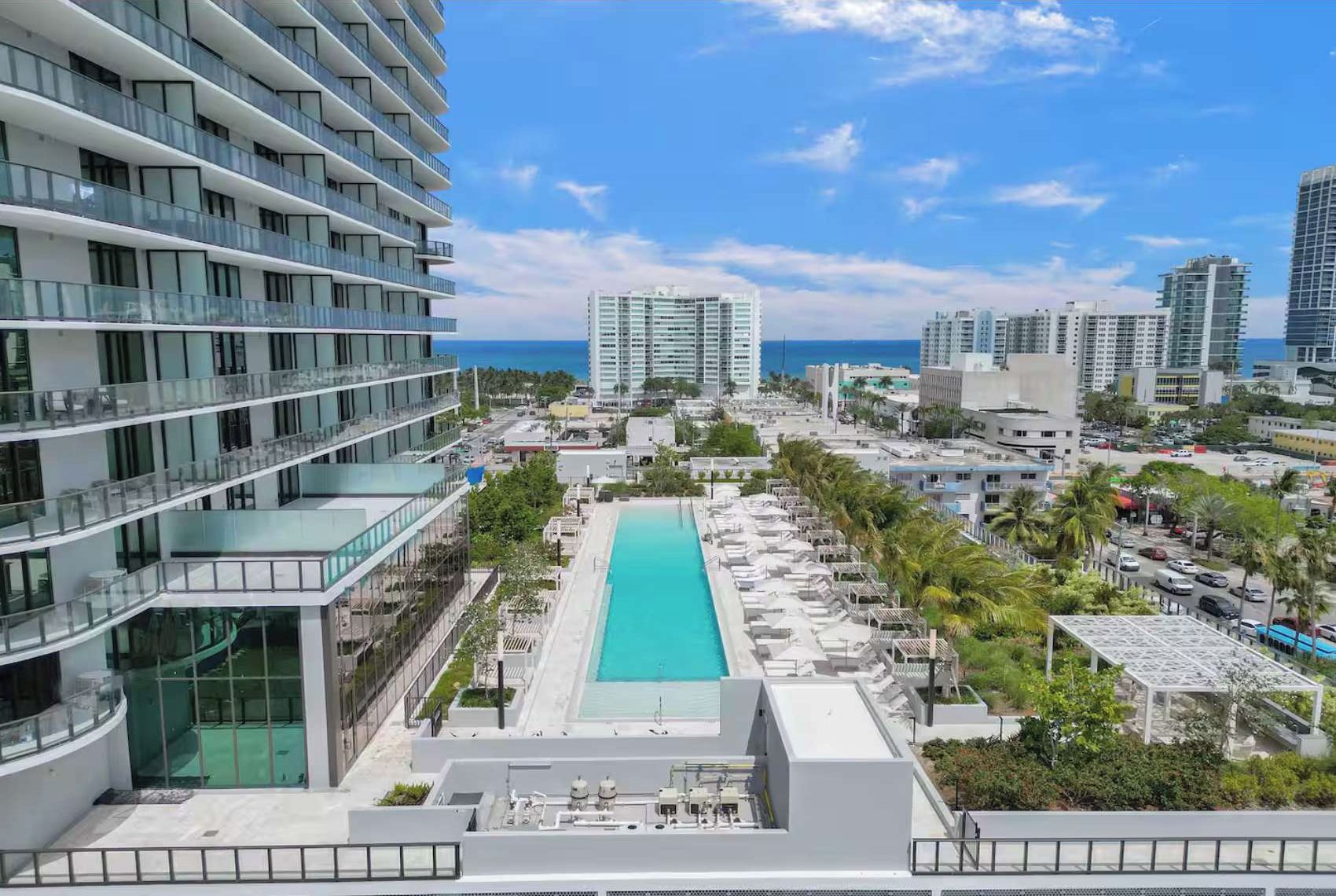 A high-rise hotel with a rooftop pool, multiple balconies, and a view of the ocean.