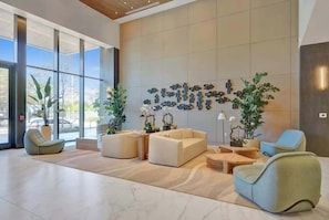Eine geräumige Lobby mit großen Fenstern, einer Sitzecke mit Sofas und Sesseln sowie dekorativen Wandbildern.